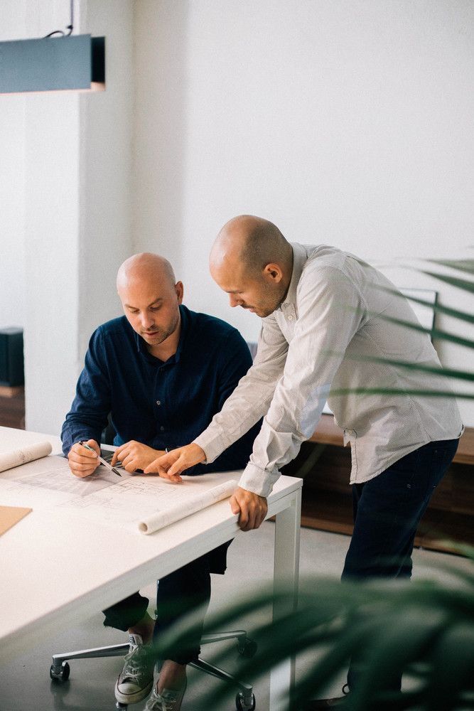 Deux professionnels analysant des plans techniques sur une table de travail dans un bureau moderne